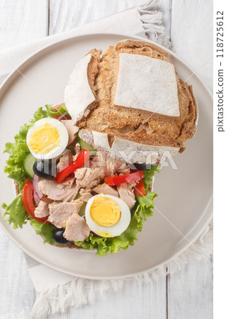 Pan bagnat is a sandwich with salad nicoise composed of raw vegetables, hard boiled eggs, anchovies and tuna closeup on the plate. Vertical top view 118725612