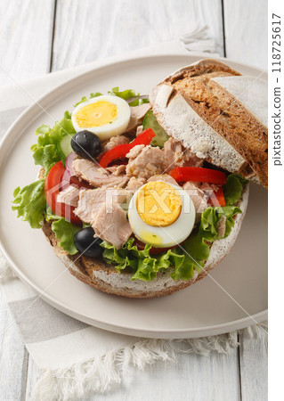Pan bagnat is a sandwich with salad nicoise composed of raw vegetables, hard boiled eggs, anchovies and tuna closeup on the plate. Vertical Pan bagnat is a sandwich with salad nicoise composed of raw vegetables, hard boiled eggs, anchovies and tuna closeup on the plate. Vertical 118725617