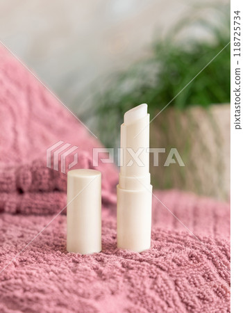 Opened lip balm stick on pink folded towel near green plant in bathroom close up, mockup 118725734
