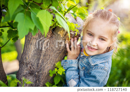 Beatiful smiling child girl hiding behind a tree in summer park Beatiful smiling child girl hiding behind a tree in summer park 118727140