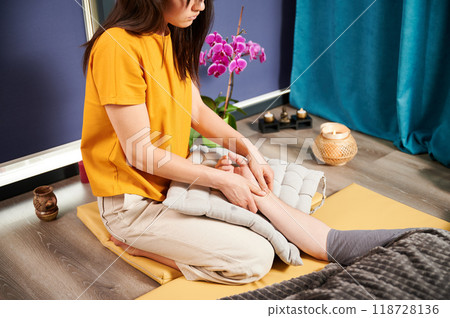 Masseuse making thai yoga massage. Cropped view of woman therapist doing traditional massage treatment for male patient indoors. Client lying on mat, enjoying hand massage in calm atmosphere. 118728136