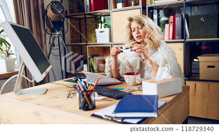 Employee stares at thermometer, looking concerned. Ignoring health symptoms for work can lead to more severe issues later. 118729340