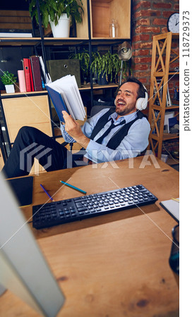 Businessman leans back with headphones on, enjoying moment, showing how getting too comfortable in office can reduce overall output. 118729373