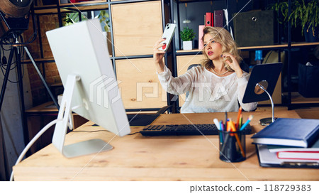 Worker posing for selfie, her attention diverted from her duties. This shows negative impact of constant phone usage during work hours. Worker posing for selfie, her attention diverted from her duties. This shows negative impact of constant phone usage during work hours. 118729383
