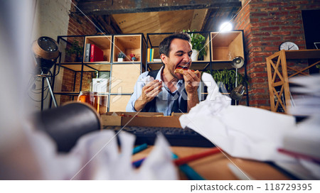 Worker eating with grin, oblivious to work chaos around him. His expression reveals lack of concern for consequences of his behavior. Worker eating with grin, oblivious to work chaos around him. His expression reveals lack of concern for consequences of his behavior. 118729395