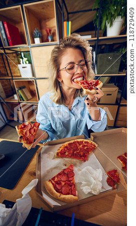 Employee eating pizza, seemingly unaware of how this habit is affecting her productivity. Messy workspace reflects poor time management. 118729409