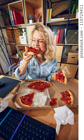 Close-up of worker biting into pizza slice, clearly distracted from task at hand. Eating during work hours shows disorganization and unprofessional behavior. 118729411