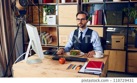 Businessman neatly sets up his desk with food. Though efficient, eating at workspace during meetings might lead to distractions. 118729431
