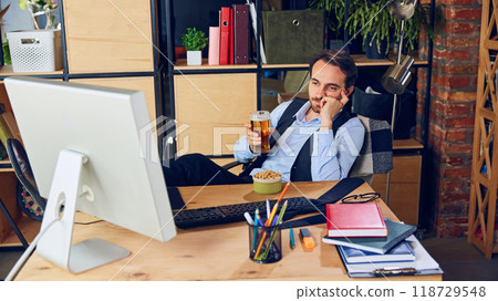 Man, professional, sitting in chair at desk with beer in frustration during workday while watching match in which his favorite sports team loses. 118729548