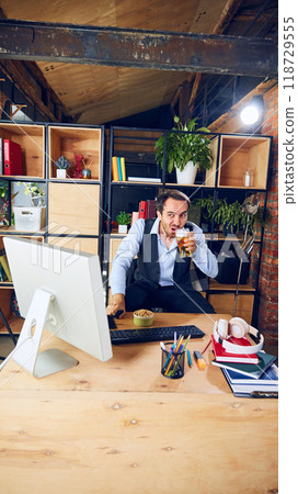 Raising glass of beer, he pauses to enjoy break during his workday, taking moment to celebrate goal by favorite football team. 118729555
