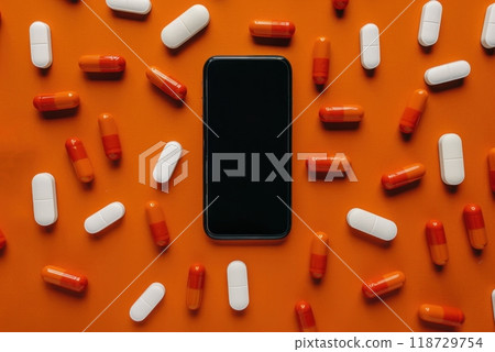 A black smartphone lies on an orange background surrounded by white and orange pills. 118729754