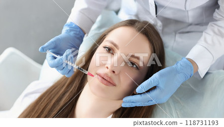 Young woman gets injection of botox in her lips, cosmetologist using syringe Young woman gets injection of botox in her lips, cosmetologist using syringe 118731193