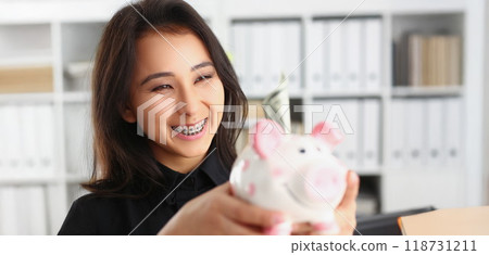 Pretty laughing young woman holding piggybank with banknote in it 118731211