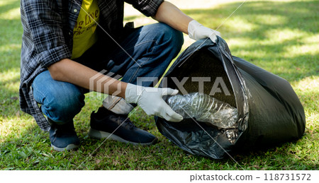 Hand holding plastic bottle waste, picking up trash and putting it in the black garbage bag at the Park on Environmental Earth day 118731572