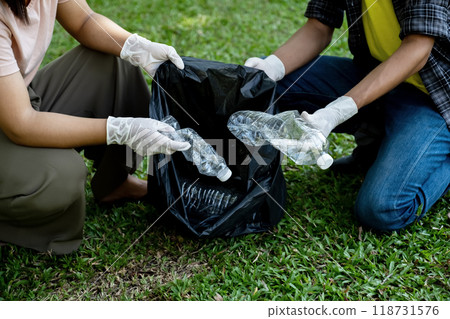 Hand holding plastic bottles waste, Couple picking up trash putting to the black garbage bag at public Park on Environmental Earth day Hand holding plastic bottles waste, Couple picking up trash putting to the black garbage bag at public Park on Environmental Earth day 118731576