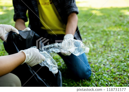 Hand holding plastic bottles waste, Couple picking up trash putting to the black garbage bag at public Park on Environmental Earth day Hand holding plastic bottles waste, Couple picking up trash putting to the black garbage bag at public Park on Environmental Earth day 118731577