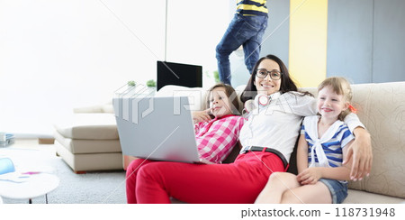 Happy woman posing with her kids on couch while working on laptop 118731948