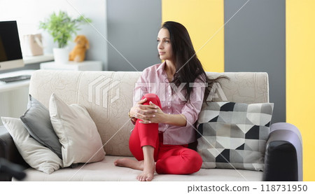 Brunette pensive young woman looking away sitting on couch at home 118731950
