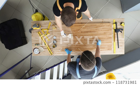 Coworkers covering wooden plank with shiny polish creative process in workshop 118731981