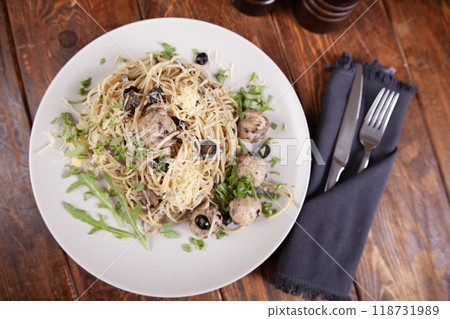 A plate of spaghetti with meatballs and olives on a wooden table 118731989