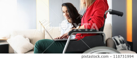 Best friends spend time together watching movie on laptop, woman in wheelchair hold device on lap Best friends spend time together watching movie on laptop, woman in wheelchair hold device on lap 118731994