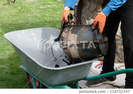 A man pours mud from a bucket into a wheelbarrow from the bottom of a well. 118732347