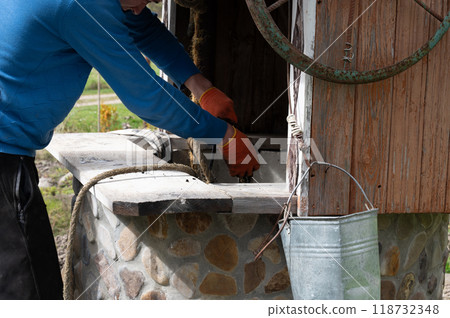 A man pulls a bucket of silt from a well with a rope. 118732348