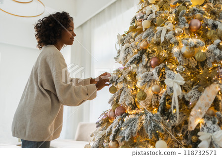 Merry Christmas. African American woman decorating Christmas tree. Happy girl near classical Christmas tree with white golden silver decorations ornament. Christmas eve at home time for celebration Merry Christmas. African American woman decorating Christmas tree. Happy girl near classical Christmas tree with white golden silver decorations ornament. Christmas eve at home time for celebration 118732571