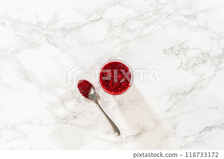 Flat lay. Freshly made Raspberry Cake Filling is carefully poured into a glass jar - ready to be used to add a burst of fruity flavor to any dessert. 118733172