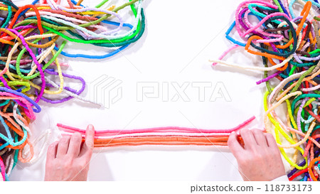 Flat lay. Hands touch a neatly organized rainbow of colorful, coiled clay bead strands against a contrasting white surface. Flat lay. Hands touch a neatly organized rainbow of colorful, coiled clay bead strands against a contrasting white surface. 118733173