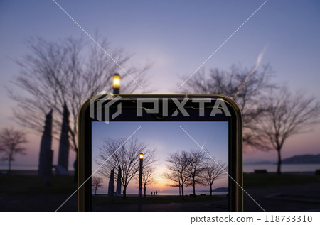 Image of a person trying to take a picture of the park scenery with a smartphone camera, where the sunset over Lake Shinji can be seen. Image of a person trying to take a picture of the park scenery with a smartphone camera, where the sunset over Lake Shinji can be seen. 118733310
