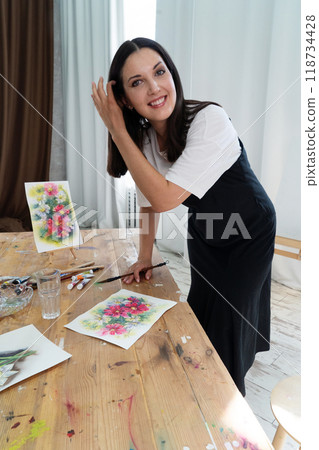 A Creative Artist is diligently at work in a bright and vibrant studio surrounded by stunning floral paintings 118734428