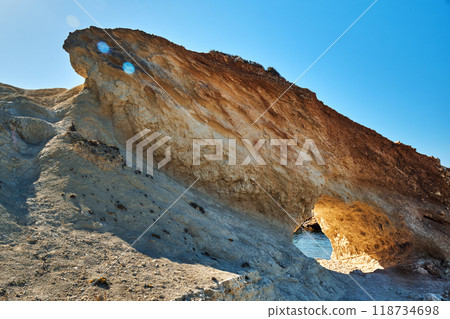 A rugged rock formation with a natural archway carved A rugged rock formation with a natural archway carved 118734698