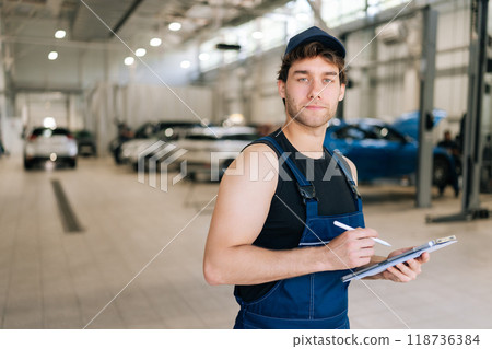 Professional supervisor mechanic male in uniform inspecting repair work checklists with tablet at garage, confident looking at camera. Concept of service car maintenance in auto transport industry. 118736384