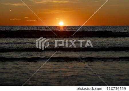 Sunrise. Dawn. Dawn in the sea. Sunrise in the sea. The first rays of sunlight rising through the sea water leaving a colorful, orange sky. Sun rays reflected in the waves of the sea. 118736539