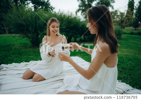 Two friends enjoy a picnic outdoors, sharing drinks in a serene park Two friends enjoy a picnic outdoors, sharing drinks in a serene park 118736705