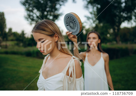 Two women in a garden during daytime with one holding a unique object 118736709