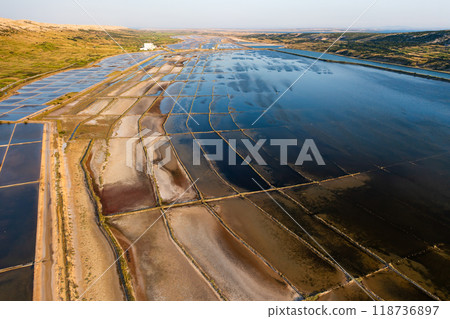 Aerial view of salt pans under the sun showcasing seawater evaporation for salt production. Aerial view of salt pans under the sun showcasing seawater evaporation for salt production. 118736897