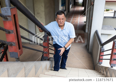 Elderly Asian man with extreme knee pain holding onto railing attempting to climb staircase Elderly Asian man with extreme knee pain holding onto railing attempting to climb staircase 118737671