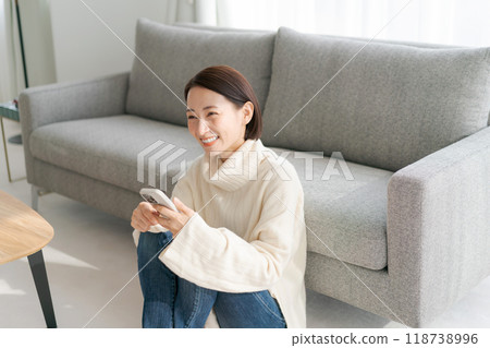 一位女士坐在客廳地板上操作智慧型手機 118738996