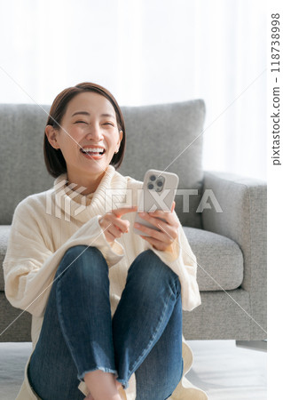 A woman sitting on the floor in the living room and using her smartphone 118738998