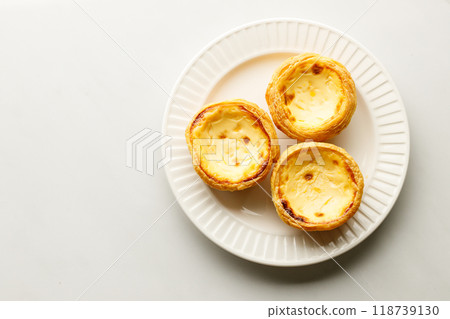 Stack of Portuguese sweet dessert egg tart or Pastel de Nata on white ceramic plate on white table. Copy space. Top view. 118739130