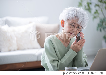 Senior woman making a phone inquiry while looking at a computer Negative image of contracts being difficult to cancel Senior woman making a phone inquiry while looking at a computer Negative image of contracts being difficult to cancel 118739191