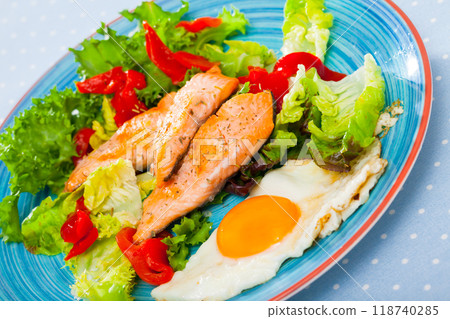 Cooked egg with fried trout, vegetables and fresh lettuce at plate on table Cooked egg with fried trout, vegetables and fresh lettuce at plate on table 118740285