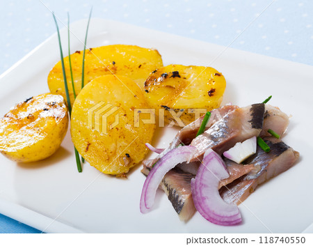 Slices of mild-cured herring with fried potatoes and onions served on plate 118740550