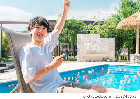 Young Asian man sitting on a recliner by the pool and playing games 118740555
