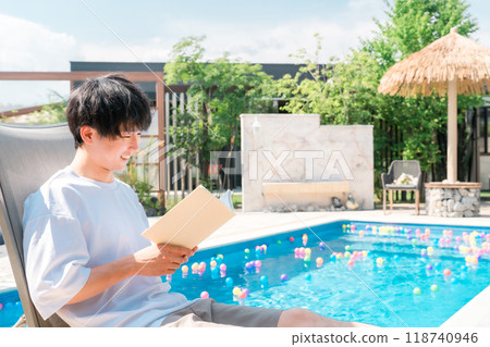 年輕的亞洲男子坐在泳池邊的躺椅上看書 年輕的亞洲男子坐在泳池邊的躺椅上看書 118740946