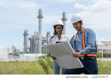 Engineer with blueprint and tablet working factory producing electricity oil energy. Engineer with blueprint and tablet working factory producing electricity oil energy. 118741477