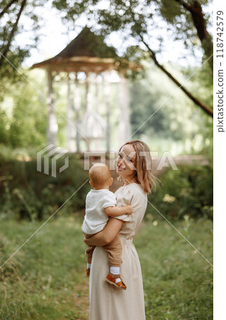 Happy woman holding a small child in her arms in the summer in a park Happy woman holding a small child in her arms in the summer in a park 118742579