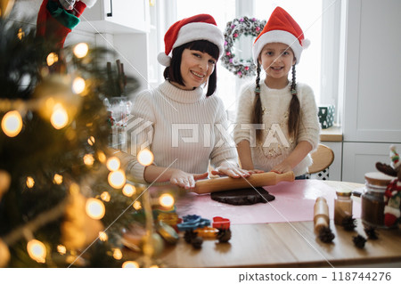 Mother and daughter baking cookies wearing Santa hats 118744276